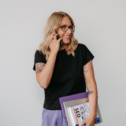Nicole von Web dir was am Telefon. Sie lacht. Dabei hält sie einen Stapel Bücher. u.a über SEO
